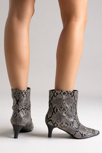 Grey snake-embossed leather ankle boots with pointed toe and kitten heel, angled view on a model's legs in studio light