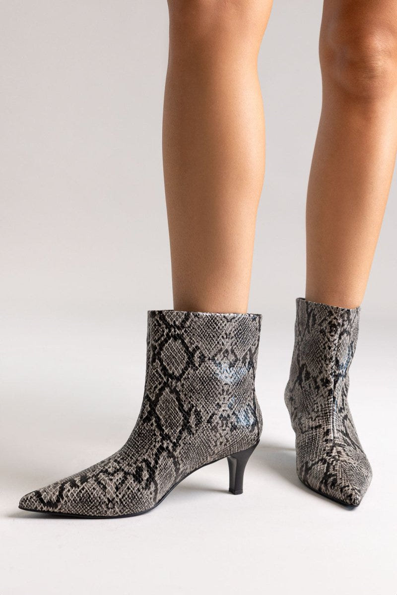 Grey snake-embossed leather ankle boots with pointed toe and kitten heel, pair in front view on a model's legs in studio light