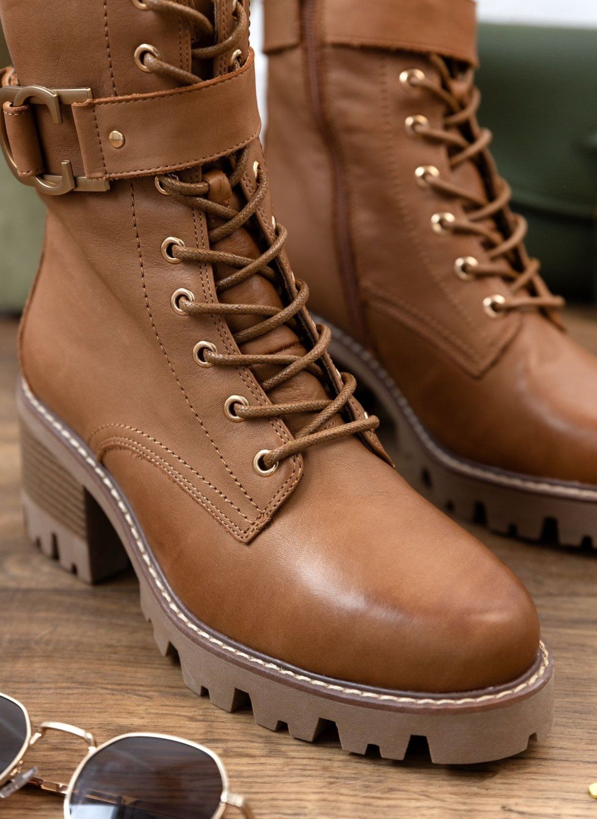 Tan leather lace-up lug-sole boot with buckle straps and block heel, close angled view on a light background