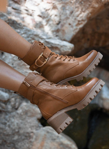 Tan leather lace-up ankle boots with buckle straps and lug sole, pair in close view on a rock background