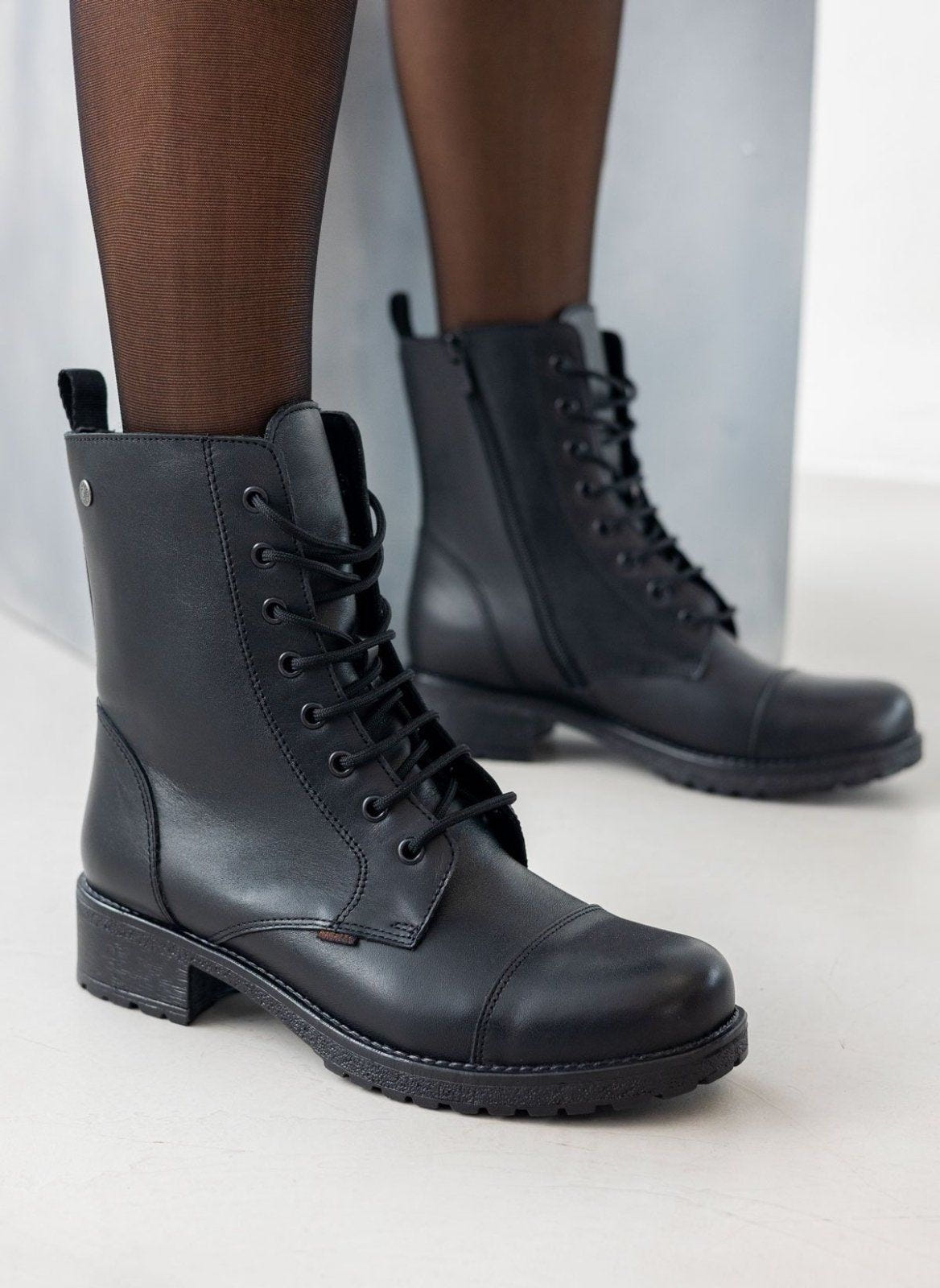 Black leather lace-up ankle boots with block heel, pair in front view on a model's legs and sheer black tights