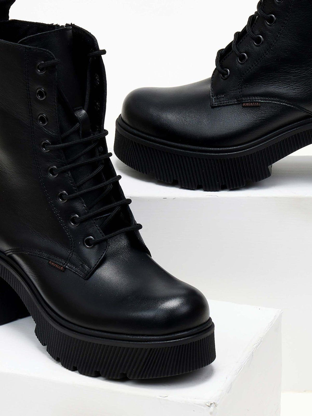 Black leather lace-up platform ankle boot with block heel, close view on a white plinth