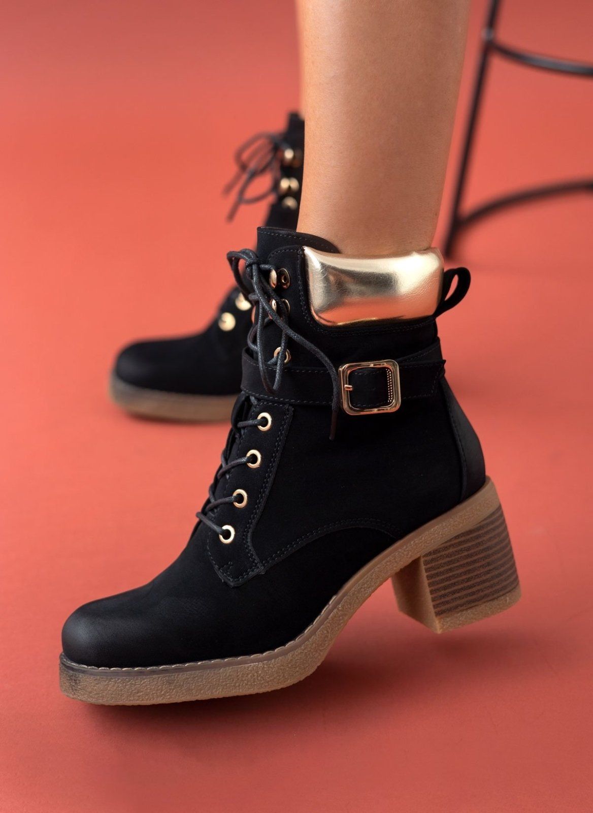 Black lace-up ankle boot with gold padded collar, buckle strap and chunky block heel, worn on model, side view