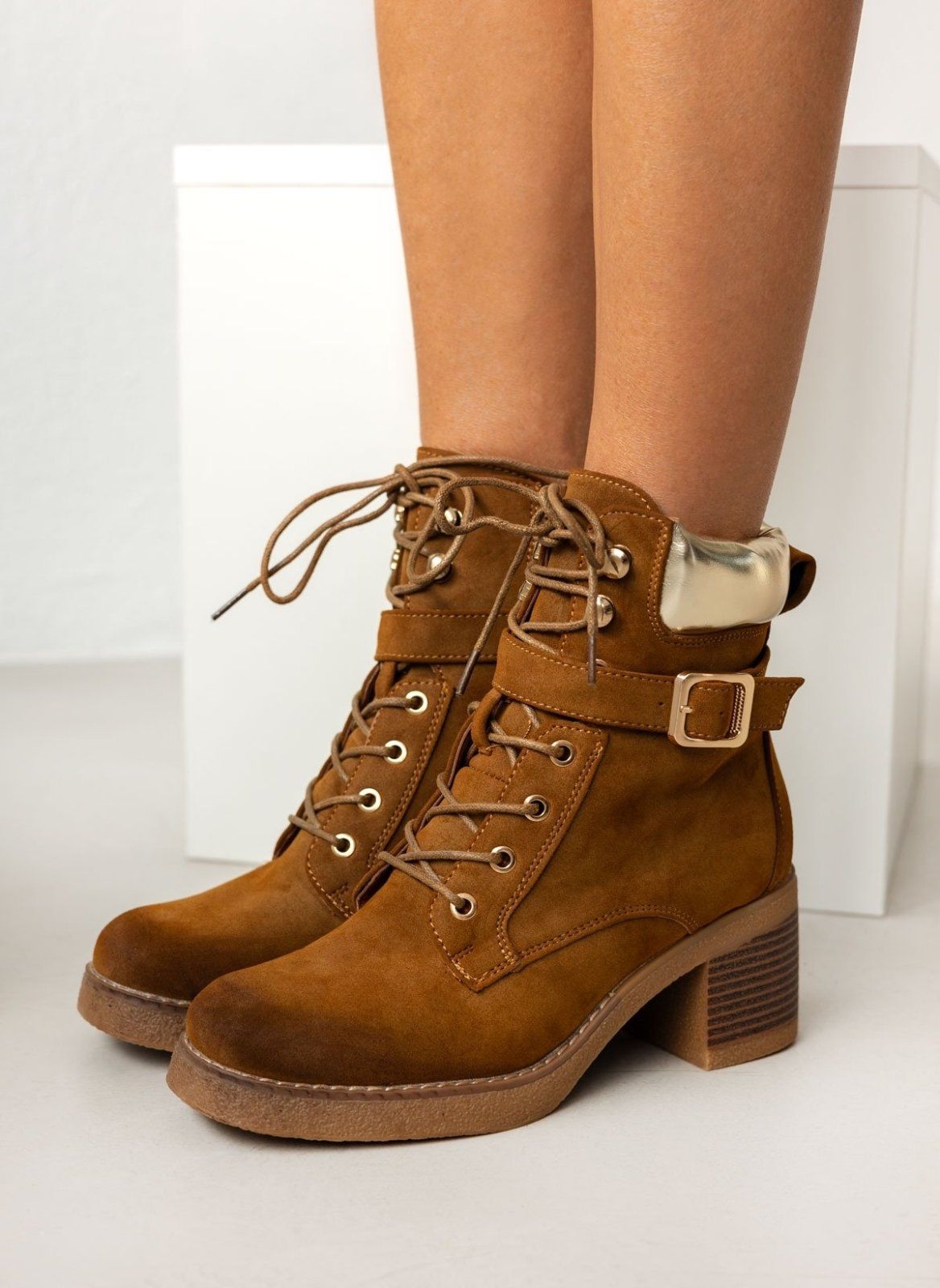 Tan suede lace-up ankle boots with gold padded collar, buckle strap and crepe sole, worn on model, front side view