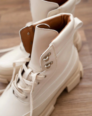 Close-up of beige faux leather lace-up ankle boot with metal eyelets, tan lining, pull tab and chunky sole, on wooden floor
