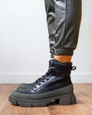 Black faux leather lace-up ankle boot with khaki green toe cap and chunky lugged sole, worn on model, side view