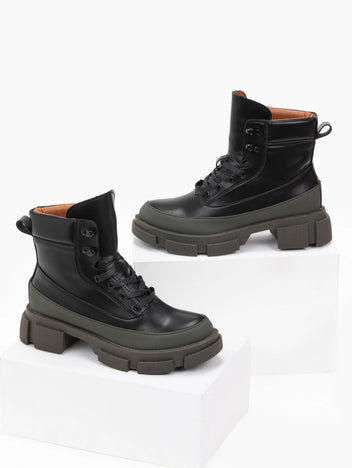 Pair of black faux leather lace-up ankle boots with khaki green toe caps, tan lining and chunky lugged soles, displayed on white blocks