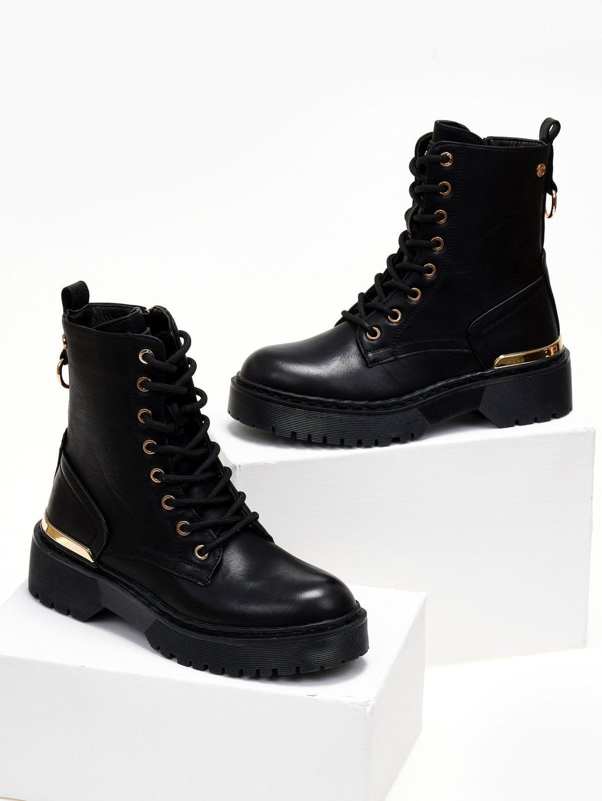 Pair of black lace-up leather boots with gold trim and chunky sole, displayed on white cubes