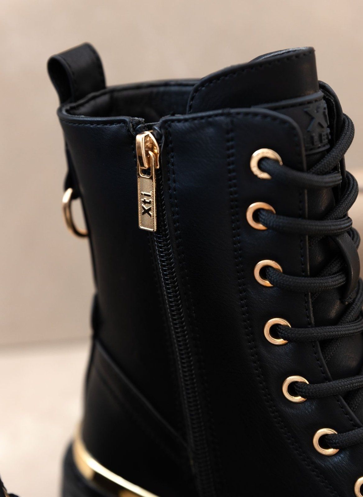 Close-up of black leather boot with gold ring eyelets, gold zip detail and lace-up front