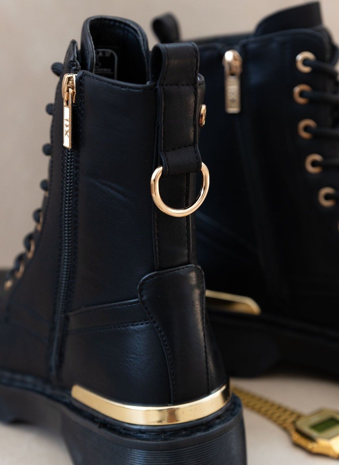 Black lace-up boots with gold ring hardware, gold trim and zip detail, shown beside gold accessories