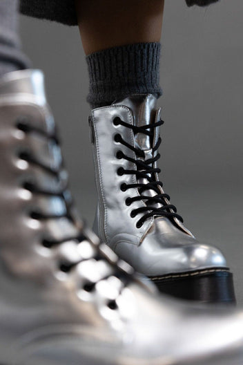 Close-up of silver metallic lace-up boot with black laces and chunky sole, shown from a low angle