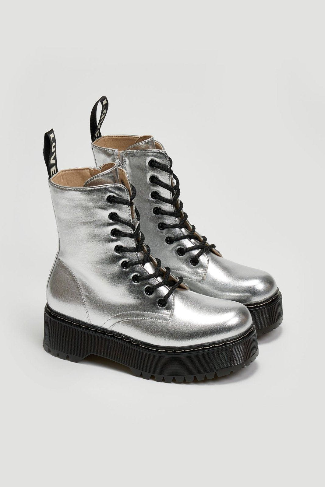 Pair of silver metallic lace-up boots with black chunky sole on a light grey background