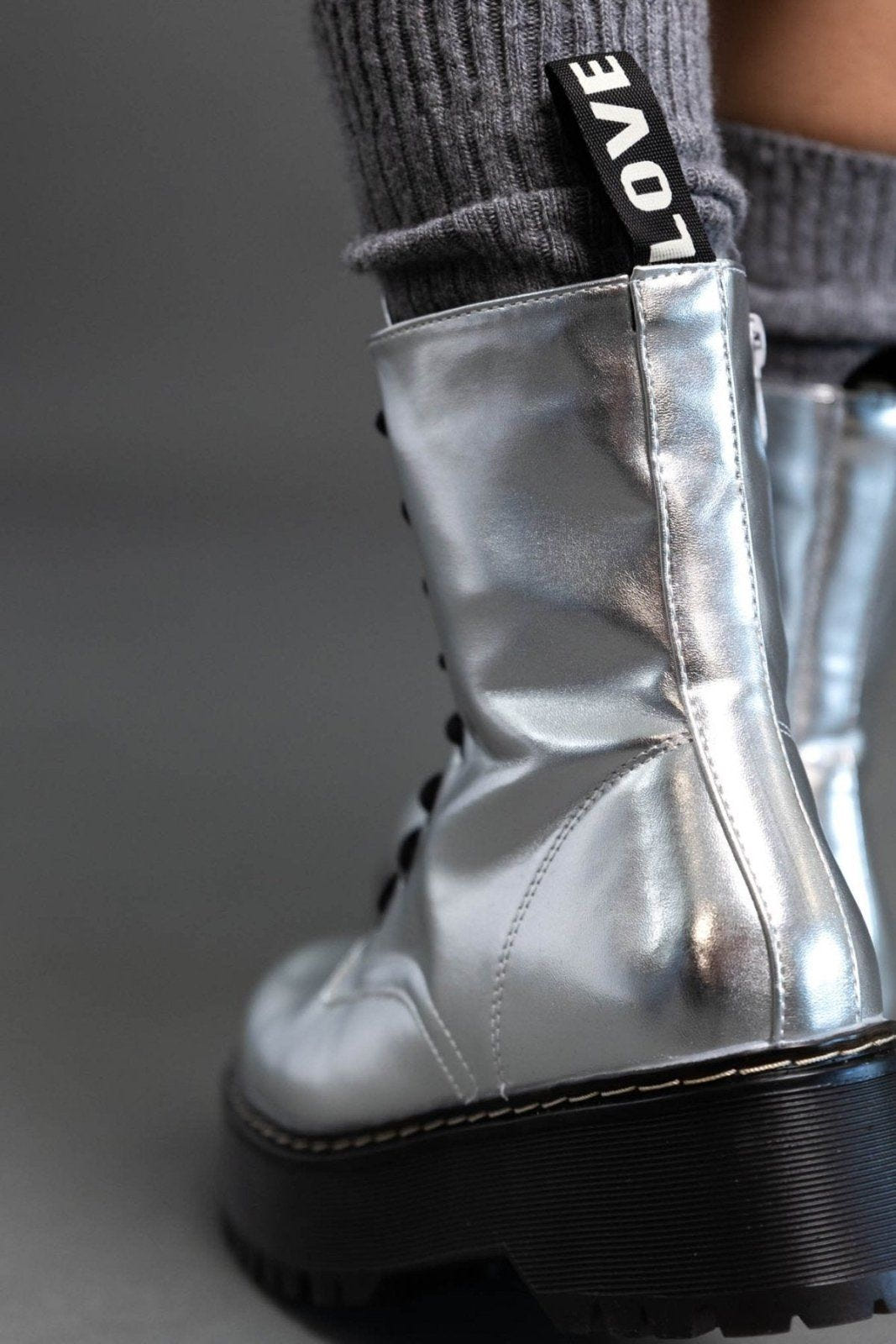 Close-up of silver metallic boot with side zip and pull tab, worn over grey knit sock