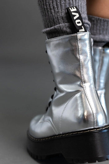 Close-up of silver metallic boot with side zip and pull tab, worn over grey knit sock