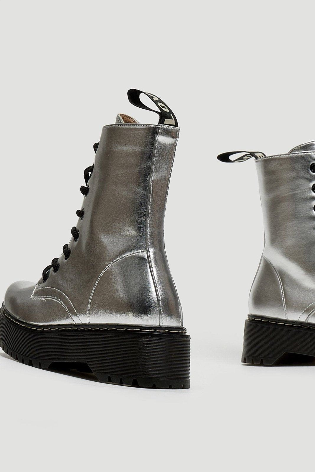 Pair of silver metallic lace-up boots with black chunky sole and pull tab, side view on grey background