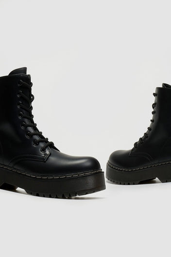 Pair of black leather lace-up boots with chunky black platform sole and white stitching, side view