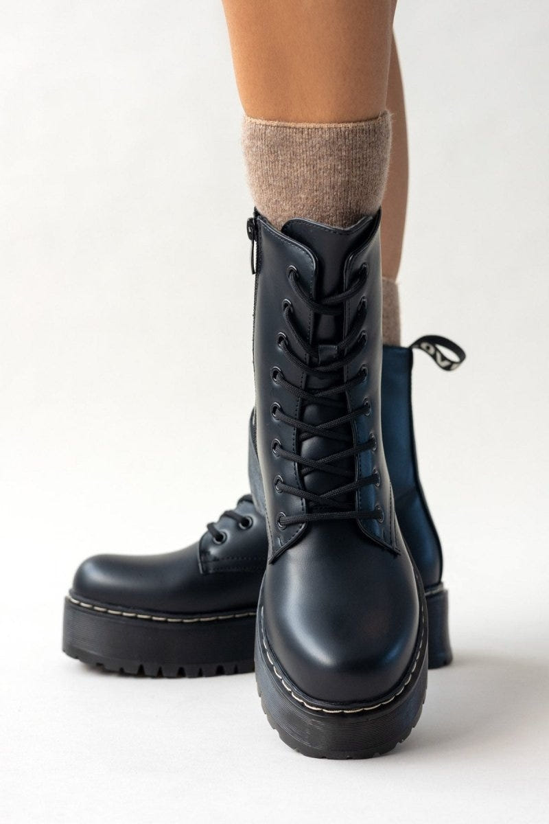 Model wearing black leather lace-up boots with chunky sole and white stitching, side view of legs