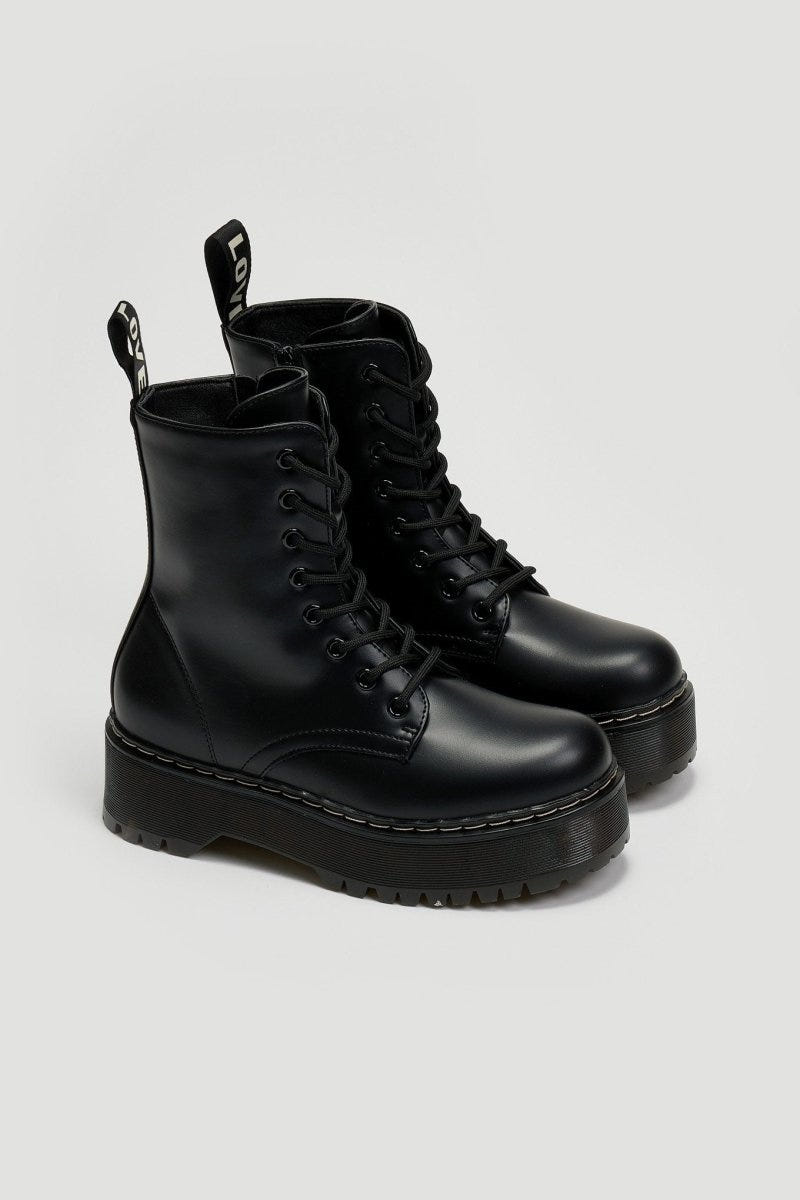 Pair of black leather lace-up boots with chunky black platform sole on a light grey background