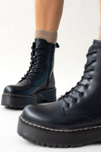Close-up of black leather lace-up boot with chunky sole and white stitching, angled view