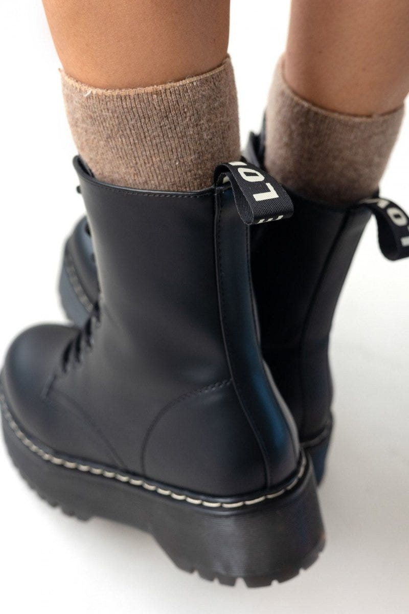 Close-up of black leather lace-up boot with chunky sole and white stitching, side view over beige socks