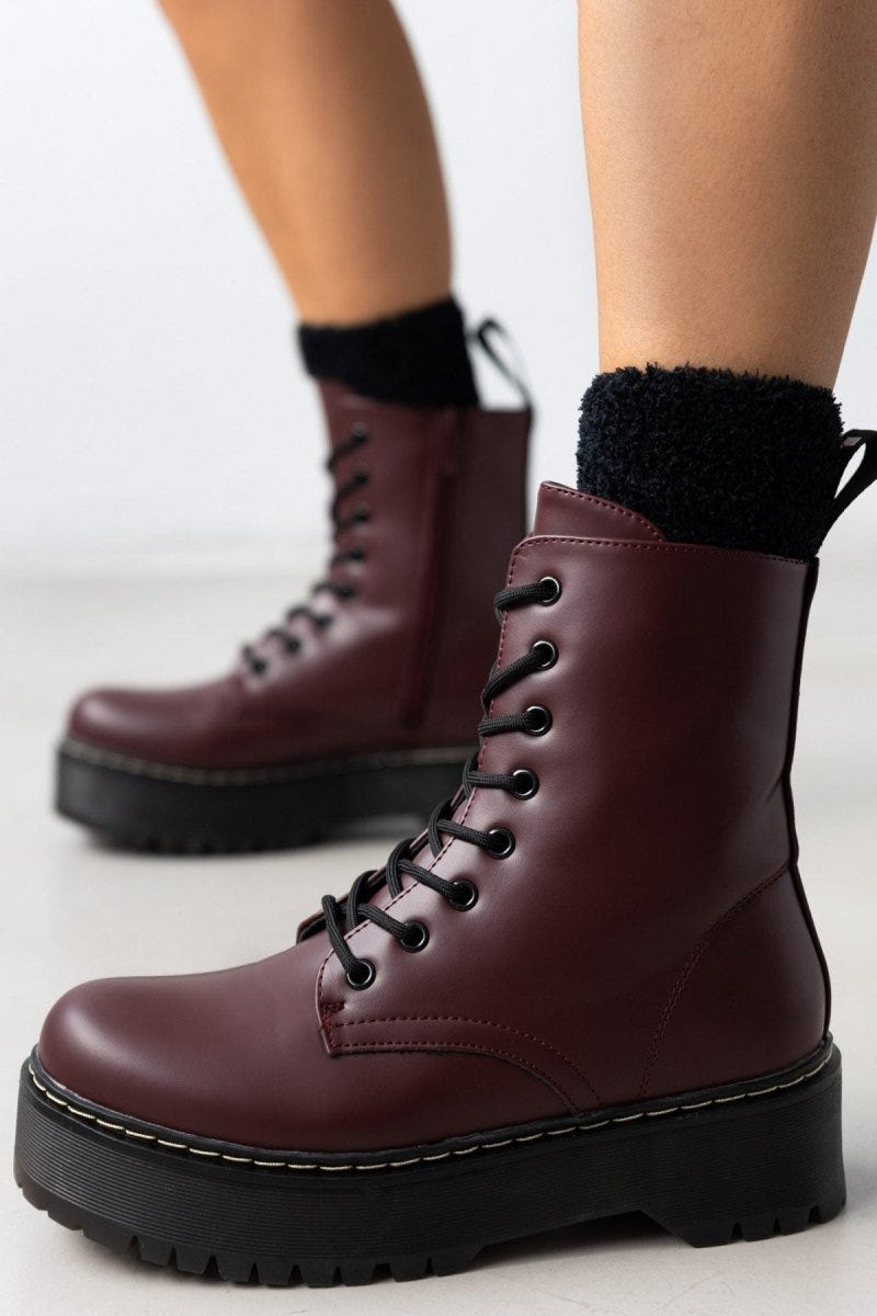 Model wearing burgundy leather lace-up boots with chunky black sole over black knit socks, front view
