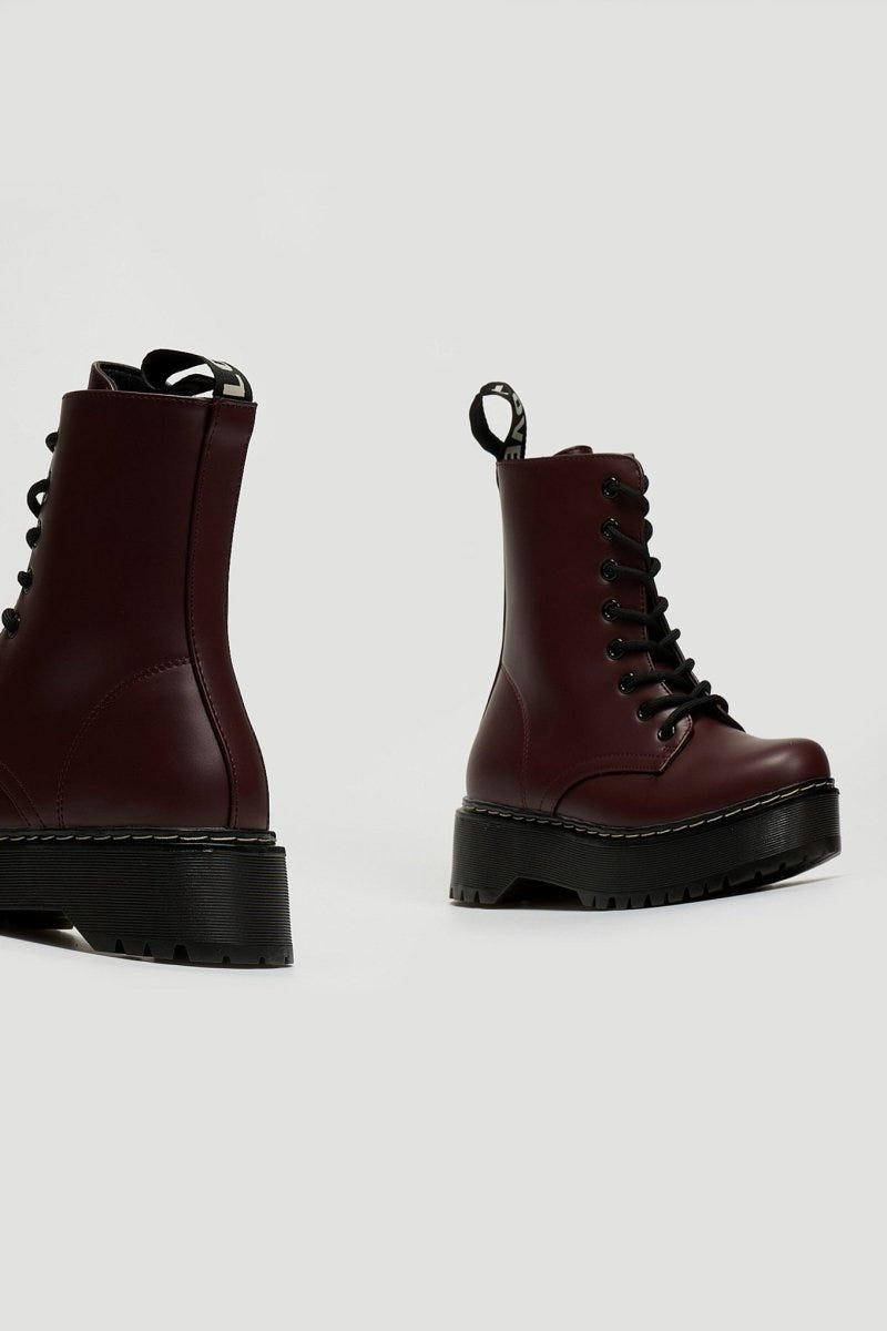 Pair of burgundy leather lace-up boots with chunky black platform sole, side view on grey background