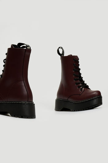 Pair of burgundy leather lace-up boots with chunky black platform sole, side view on grey background