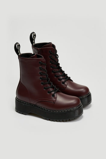 Pair of burgundy leather lace-up boots with chunky black platform sole and pull tab on grey background
