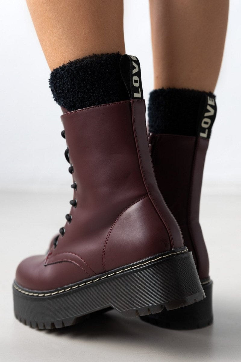 Model wearing burgundy leather lace-up boots with chunky black sole and black knit socks, close-up