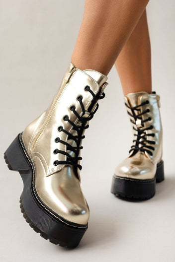 Model wearing gold metallic lace-up boots with black laces and chunky black sole, angled view