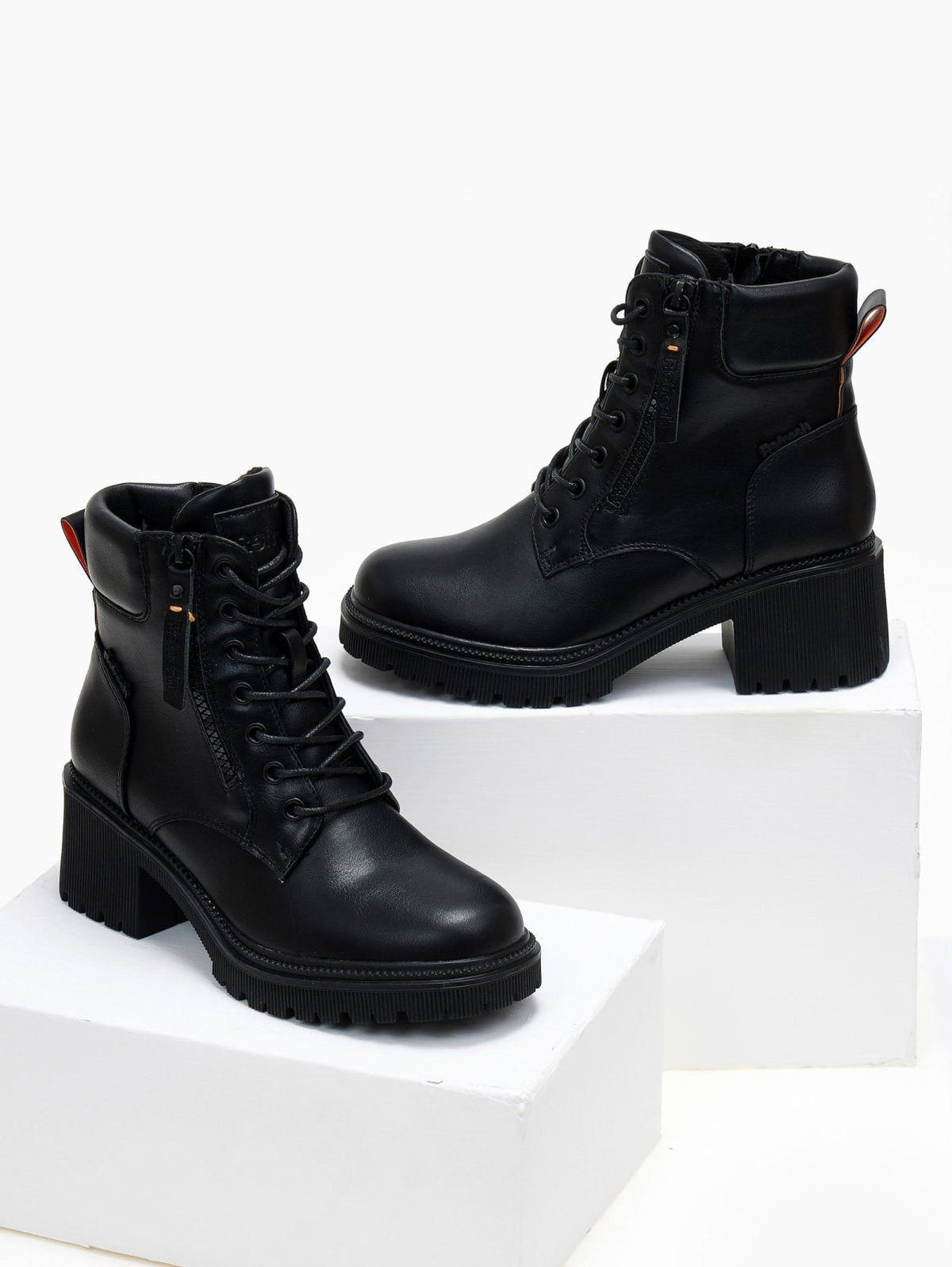 Pair of black leather lace-up ankle boots with block heel and chunky sole, styled on white display blocks