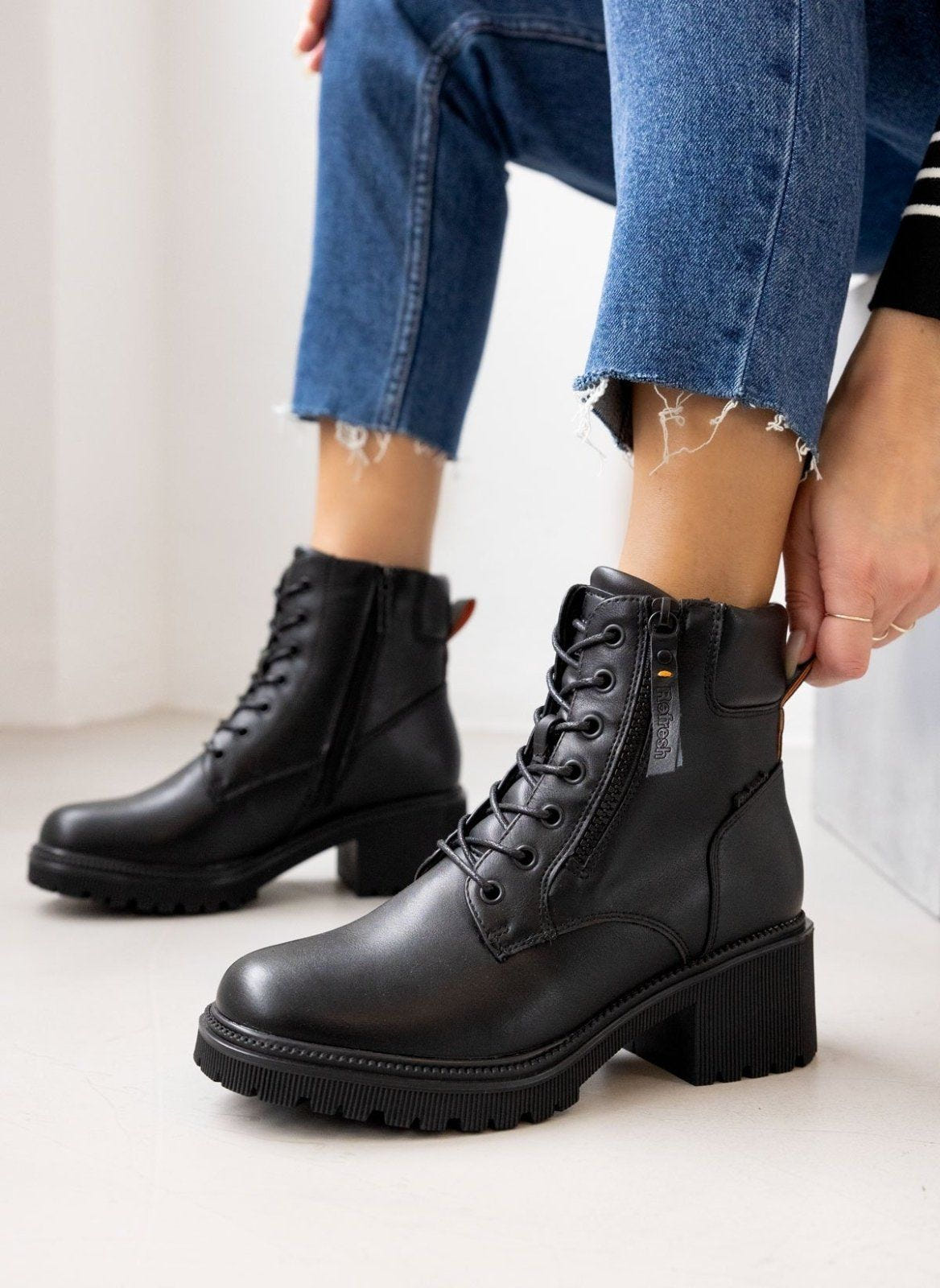 Model wearing black leather ankle boots with block heel and zip detail, styled with blue jeans