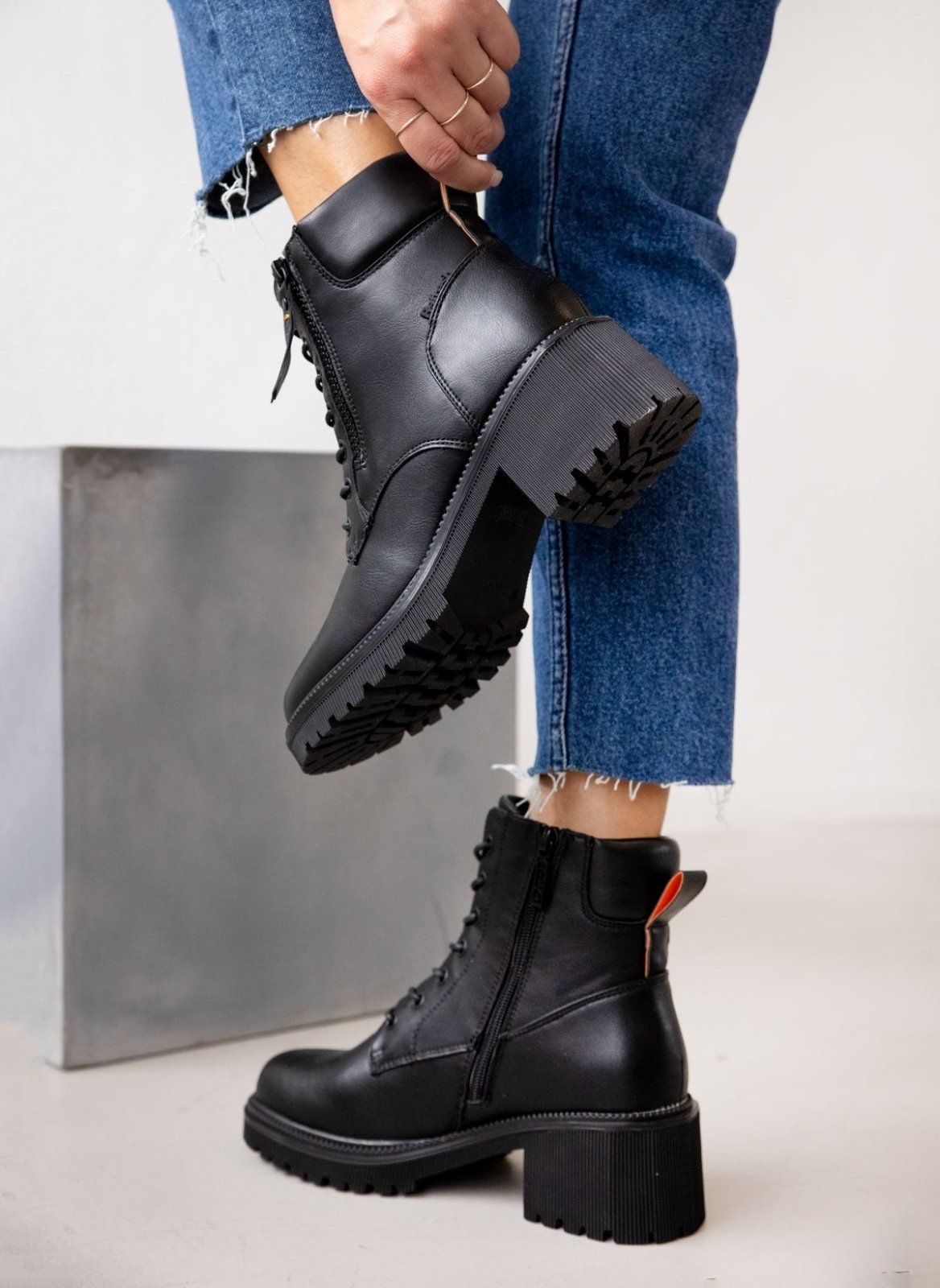 Model wearing black leather lace-up ankle boot with block heel, chunky sole and zip, styled with blue jeans
