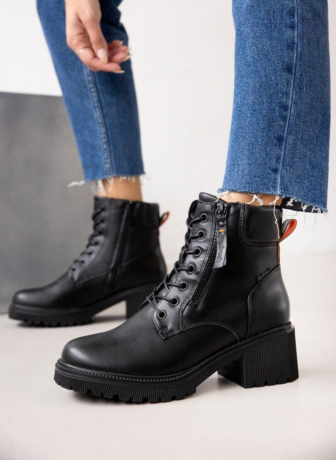 Model wearing black lace-up ankle boots with block heel and chunky sole, styled with blue jeans