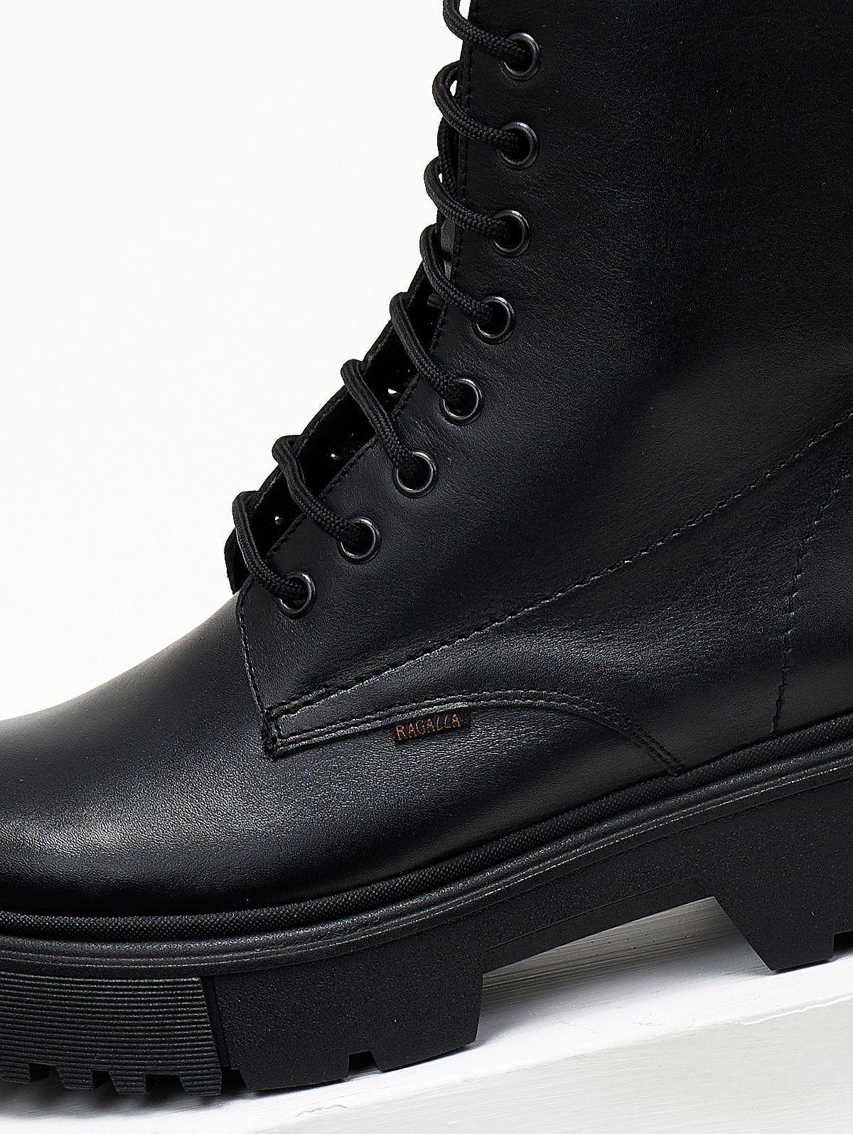 Black leather lace-up ankle boot with lug sole, close view of the lacing and sole on a light background