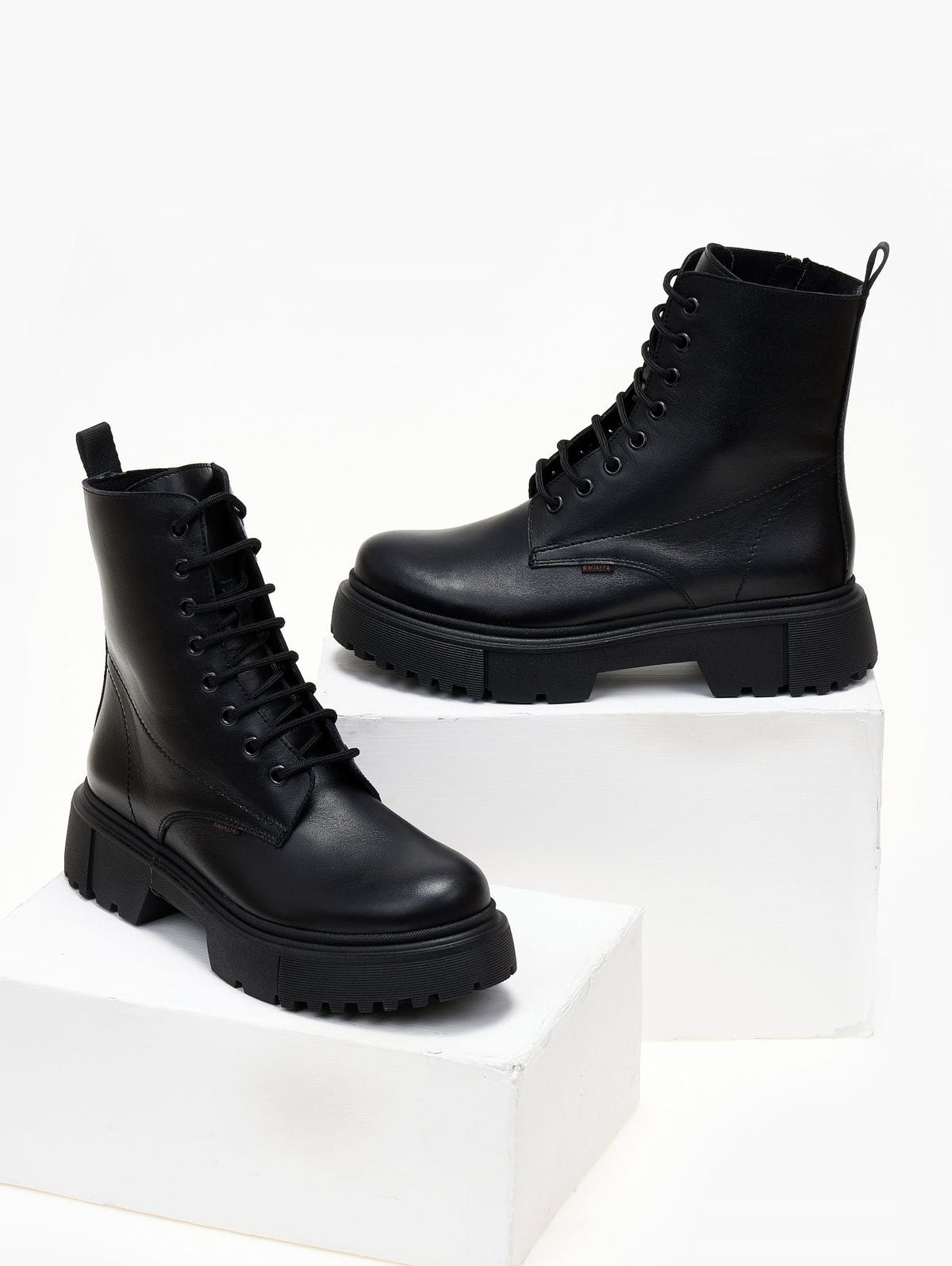 Black leather lace-up ankle boots with cap toe and lug sole, pair in angled view on a white plinth