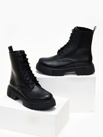 Black leather lace-up ankle boots with cap toe and lug sole, pair in angled view on a white plinth