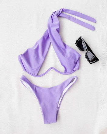 Lilac halter bikini with cutout detail and tie straps laid flat on a white background beside sunglasses