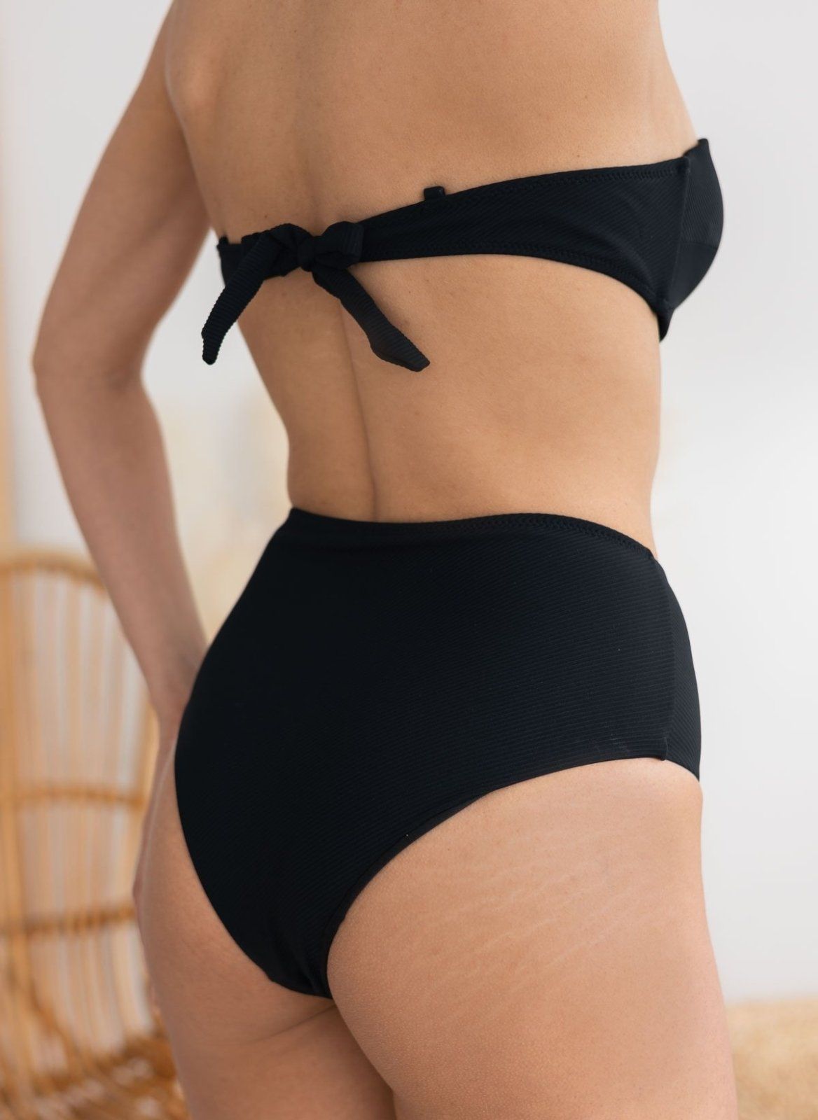 Model seen from behind wearing black bikini top with tie back and black high-waist bikini bottom