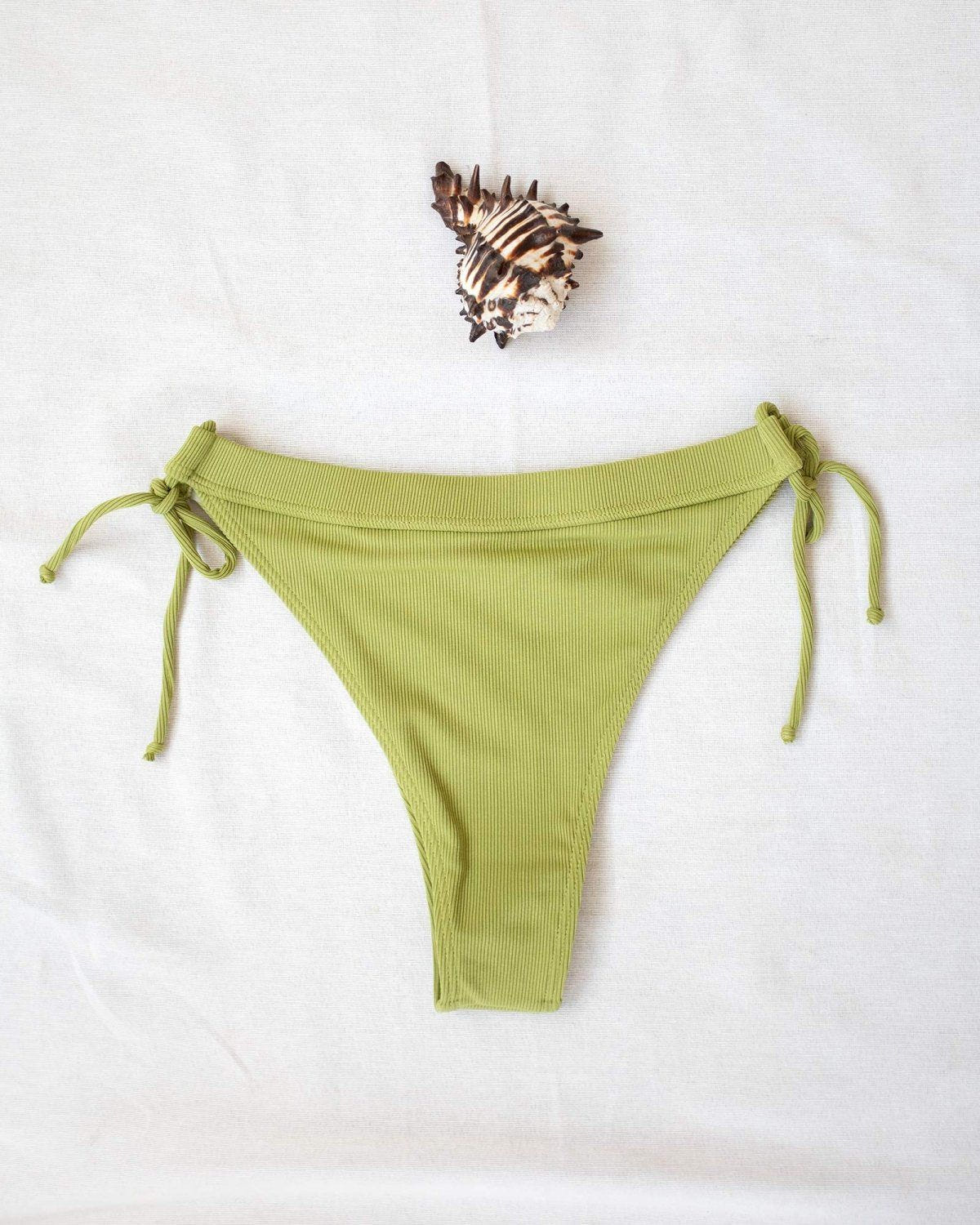 Lime green ribbed side-tie bikini bottom with tie straps, laid flat on white background beside a seashell