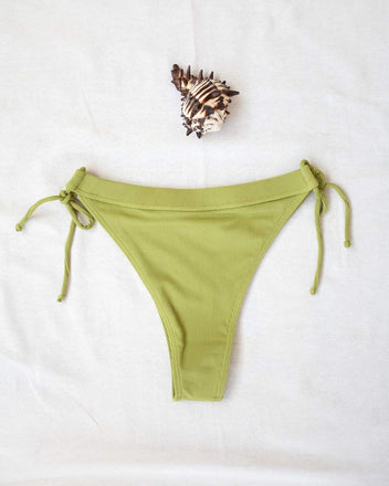 Lime green ribbed side-tie bikini bottom with tie straps, laid flat on white background beside a seashell
