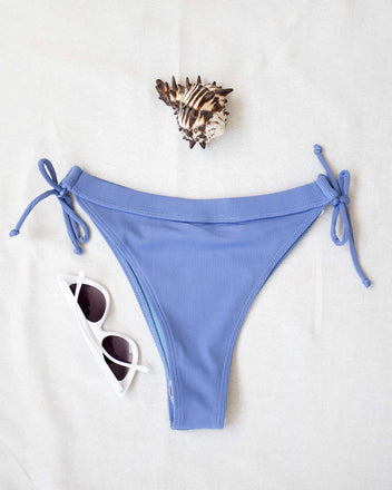 Periwinkle blue ribbed side-tie bikini bottom with tie straps, laid flat on white background beside sunglasses