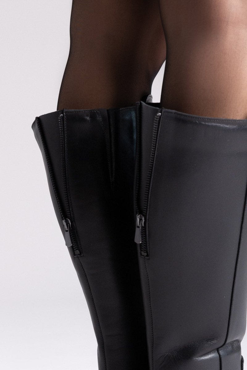 Black leather knee-high boots with side zip and block heel, close-up of legs, rear angled view