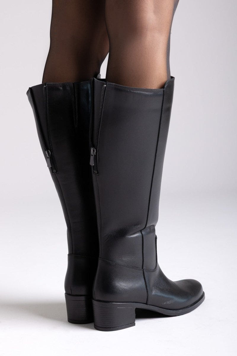 Black leather knee-high boots with side zip and block heel, close-up of legs, side view