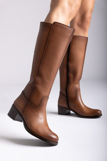 Tan leather knee-high boots with side zip and block heel, side view, model legs on grey backdrop