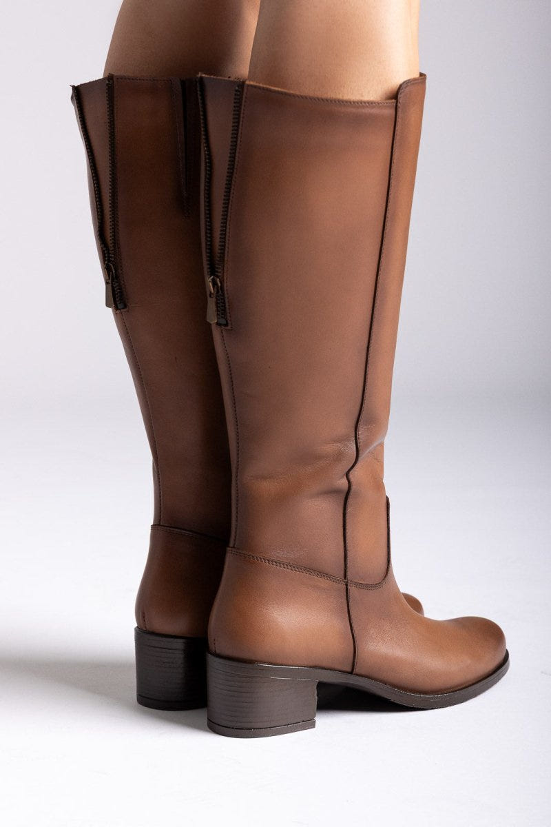 Tan leather knee-high boots with side zip and block heel, angled view on light grey backdrop