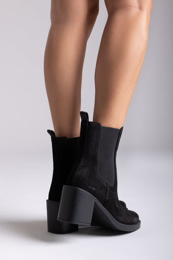 Model legs wearing black suede Chelsea ankle boots with block heel and elastic side panels, close-up