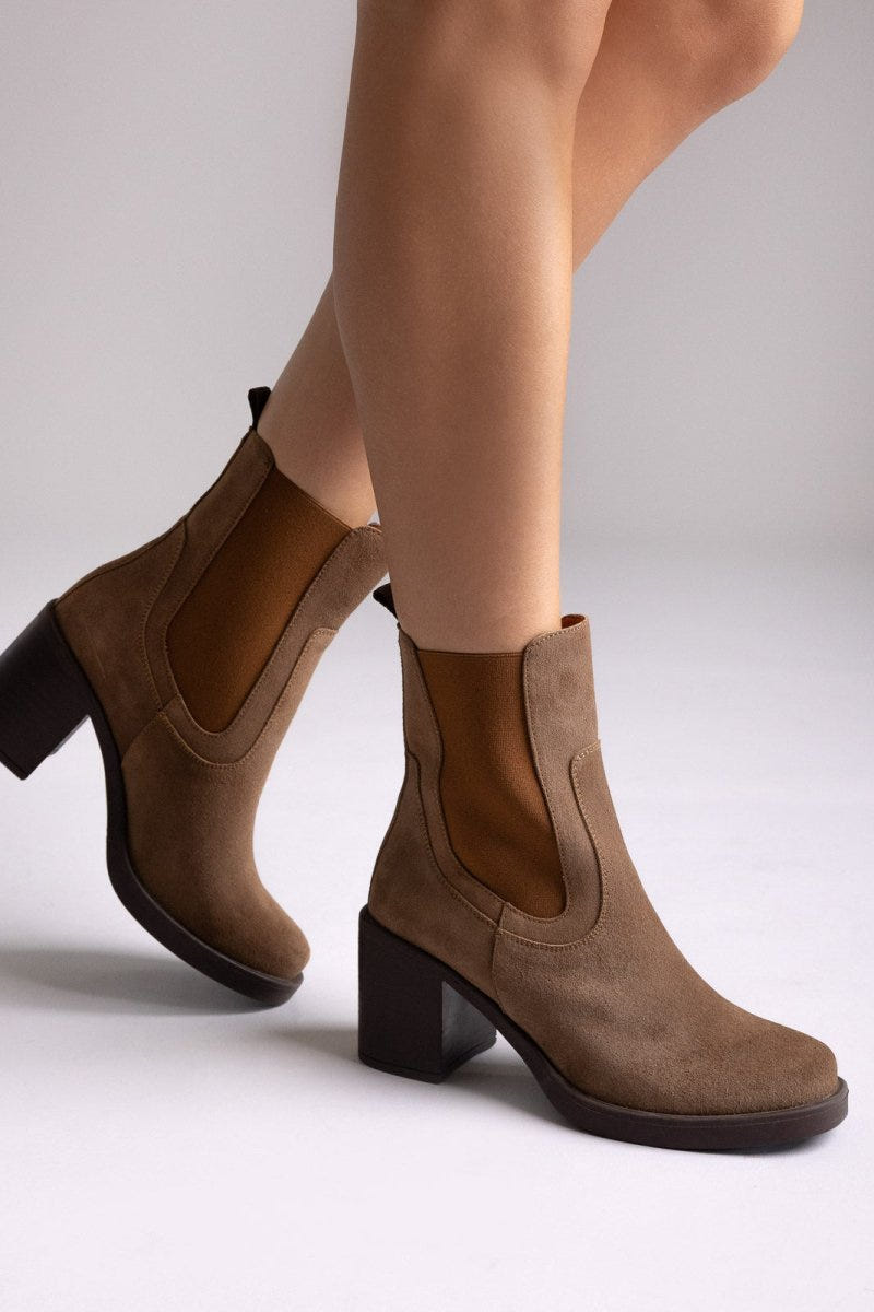 Model legs wearing tan suede Chelsea ankle boots with block heel and elastic side panels, close-up, side view