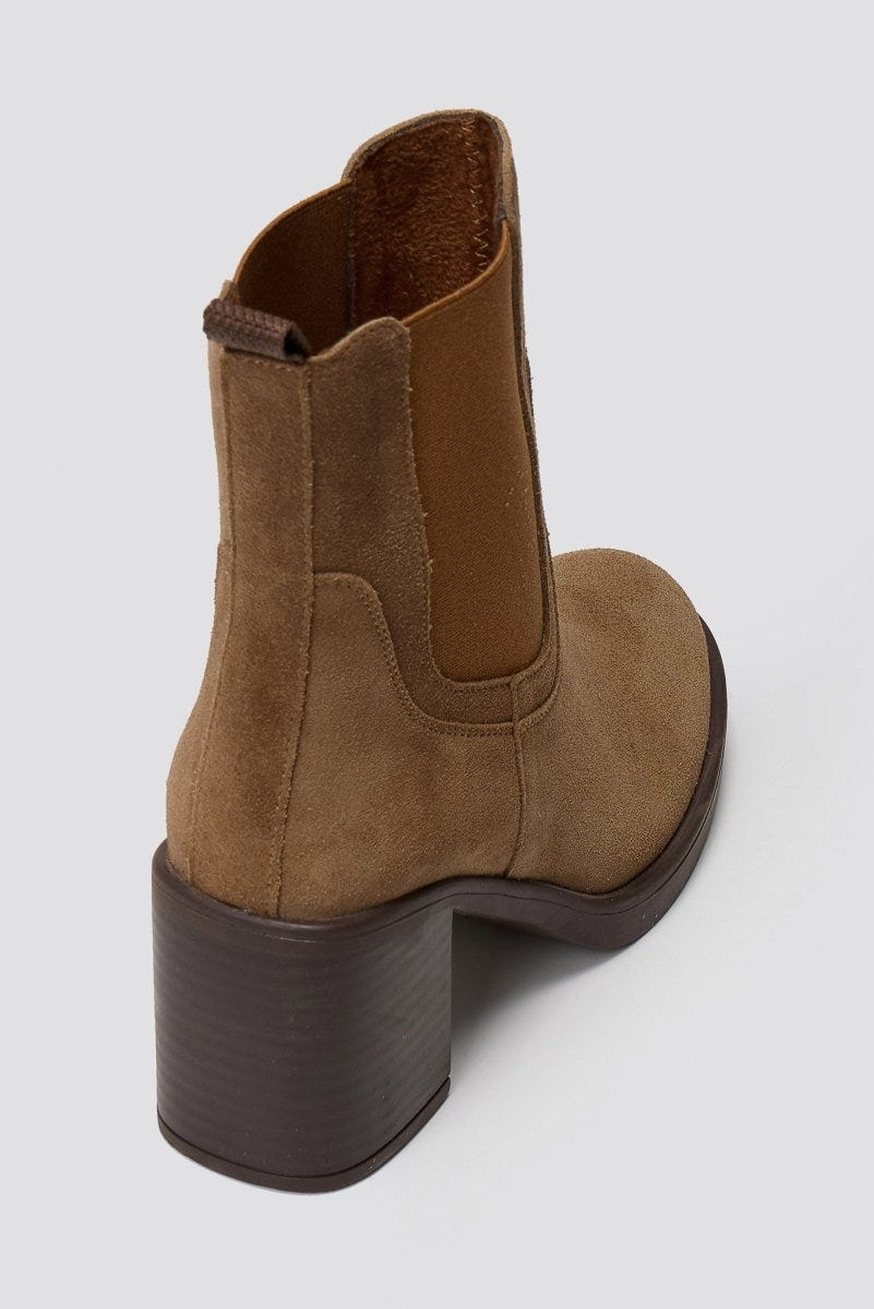 Tan suede Chelsea ankle boot with block heel and elastic side panel, angled view on grey backdrop