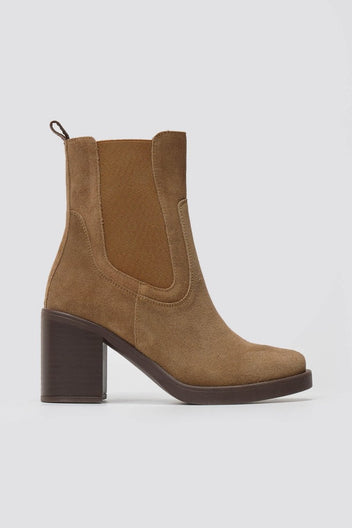 Tan suede Chelsea ankle boot with block heel and elastic side panel, side view on grey backdrop